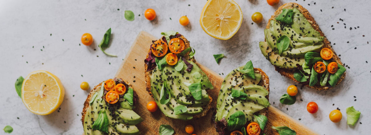 Avocado toast topped with tomatoes, greens, and seeds arranged on a wooden board.
