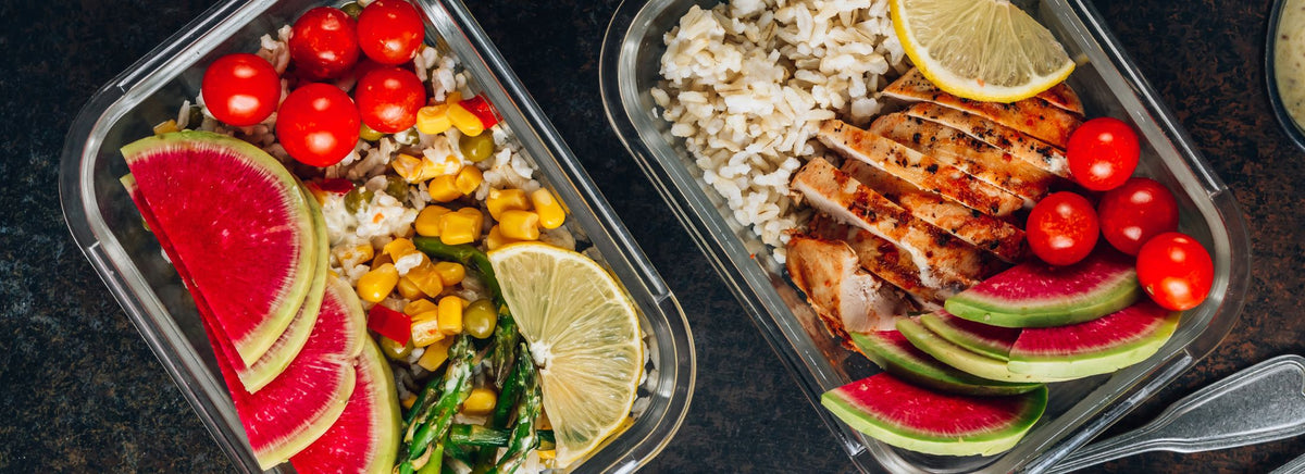 Two meal prep glass containers filled with grilled chicken, rice, corn, radish, and lime.