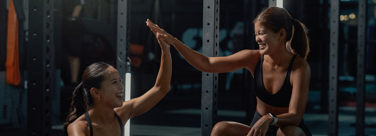 Two women in athletic wear high-fiving each other during a workout in a gym.