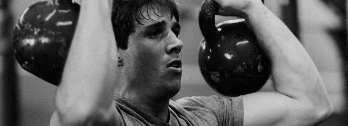 Athletic man lifting a kettlebell overhead during an intense workout.