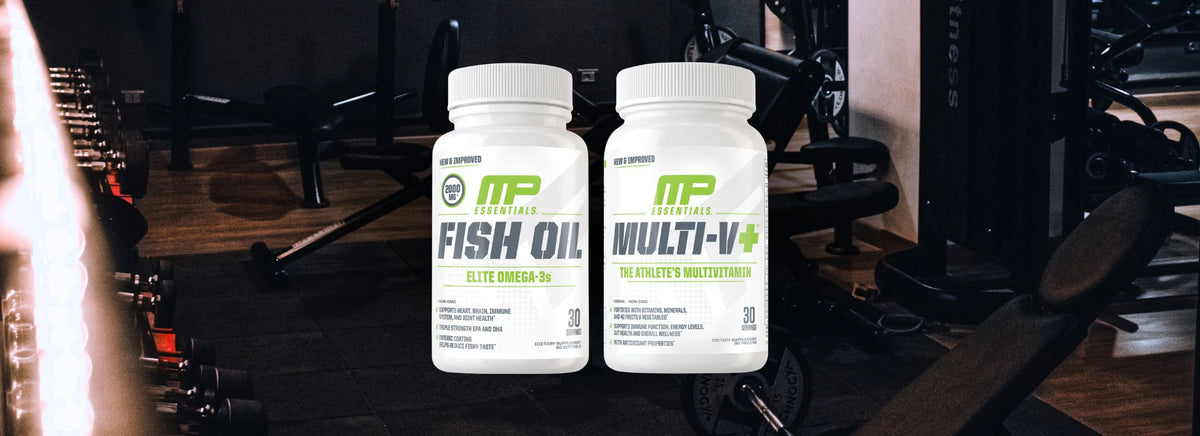 Two MusclePharm Essentials supplement bottles, Fish Oil and Multi-V+, side-by-side in a gym.