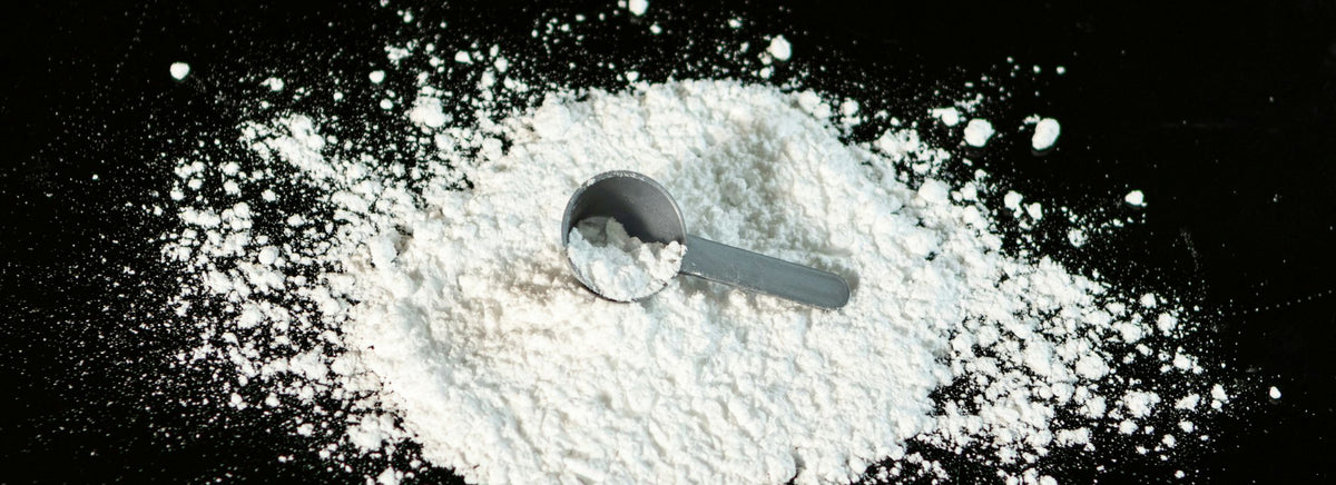 Scoop of white protein powder on a black surface with powder scattered around.