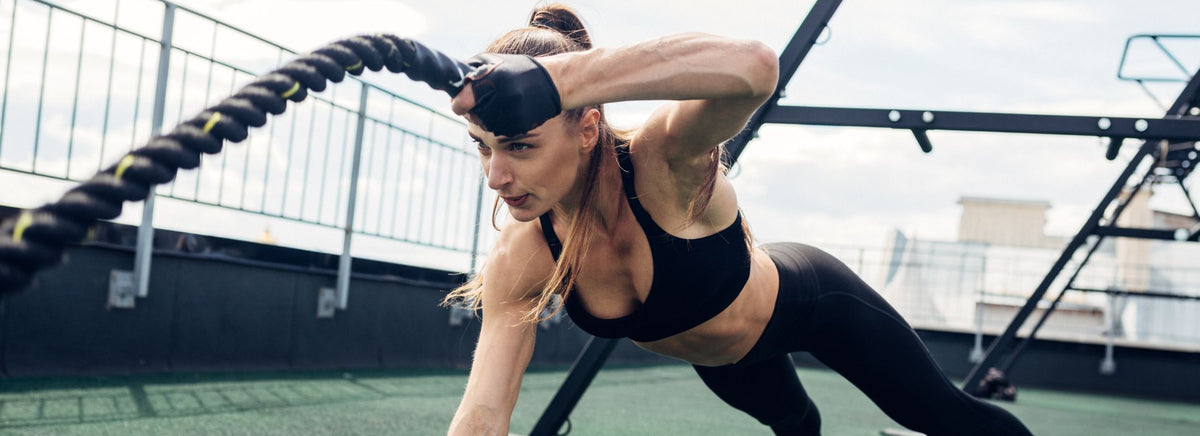 Woman in sports bra doing heavy battle rope training outdoors.