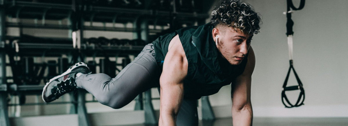 Athletic man doing a dynamic push-up or mountain climber exercise on a gym floor.