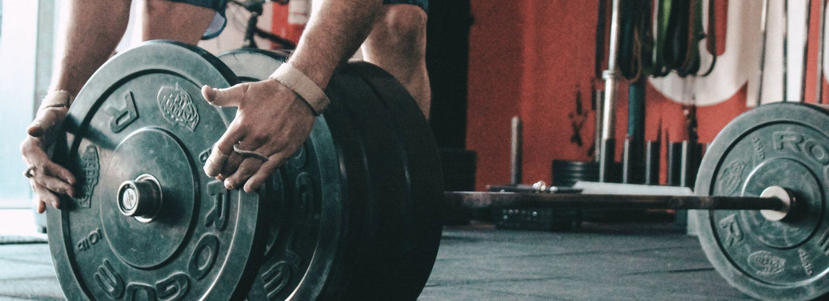 Close-up of an athlete's hands adjusting black weight plates on a barbell in a gym.