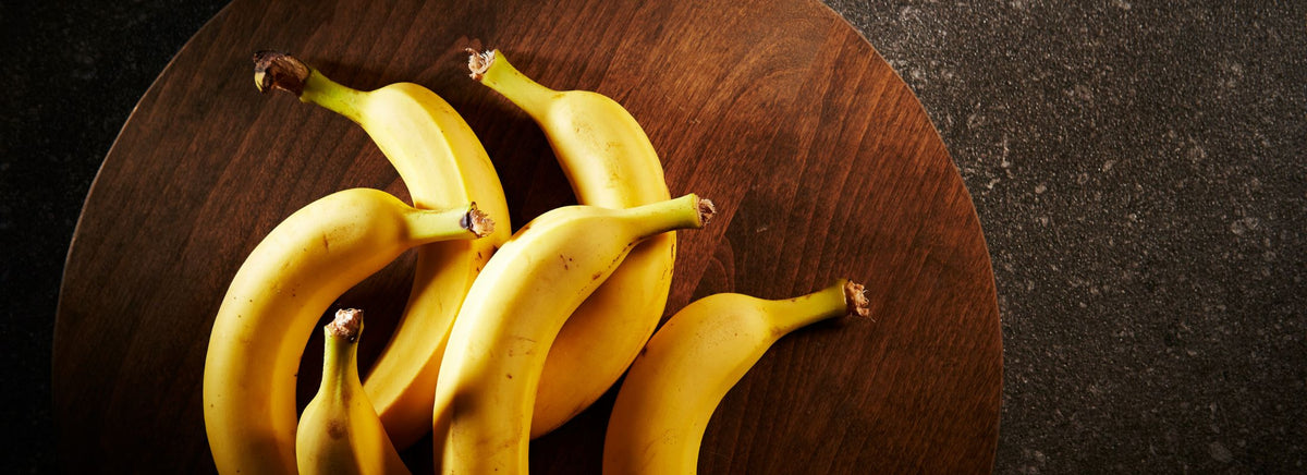 A bunch of fresh yellow bananas on a dark wooden board.