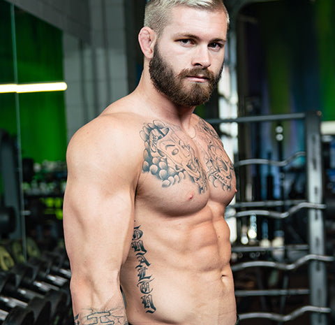 Shirtless, tattooed Jiu-Jitsu athlete Gordon Ryan posing in a gym.