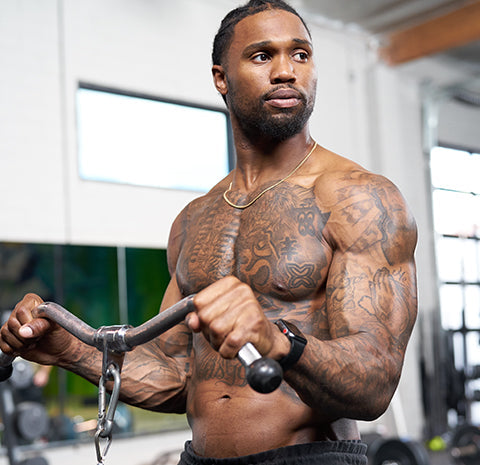 Muscular athlete Omar Bolden performing a cable bicep curl workout in a gym.